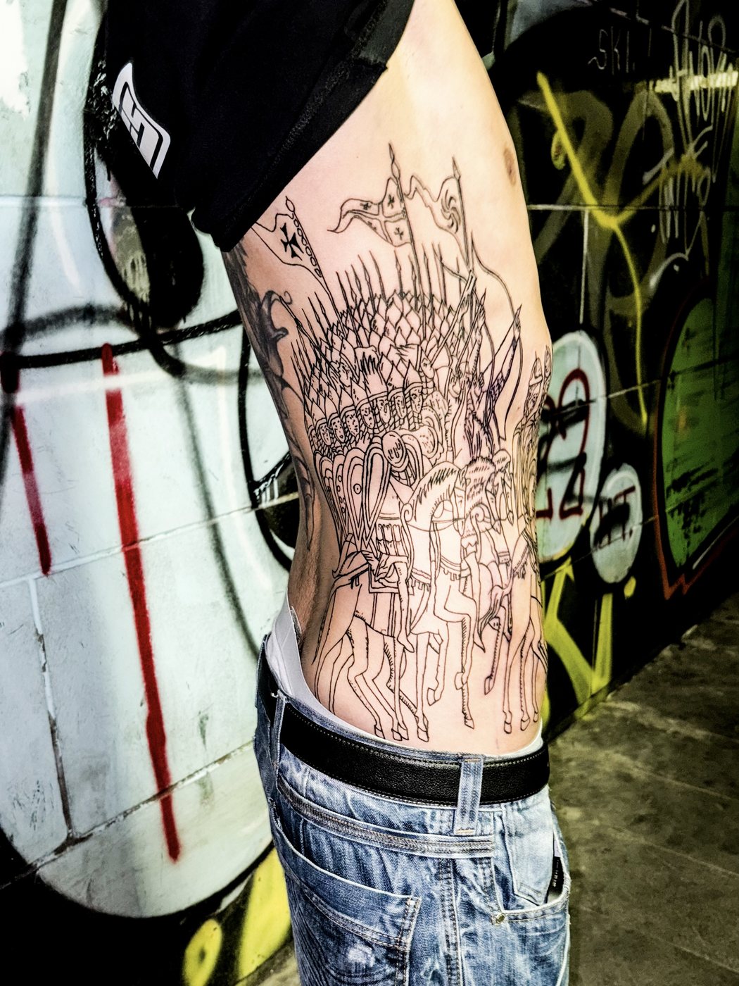 horsemen rib tattoo, side view against a graffiti wall